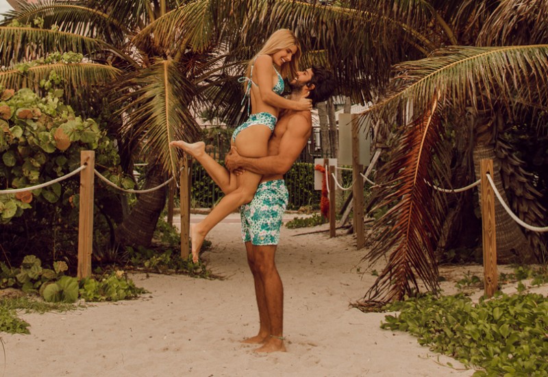 man holding woman in matching swimsuits outside in the sand