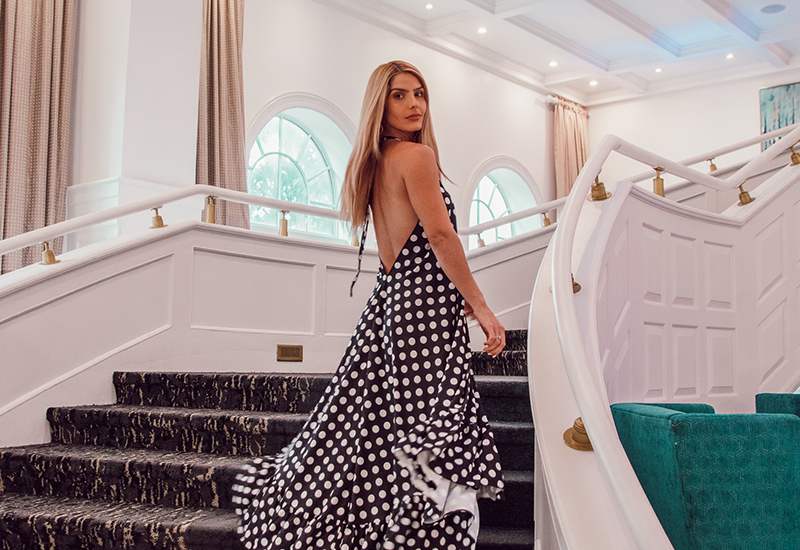 woman in a long dress walking up the white carpeted stair case while looking behind her