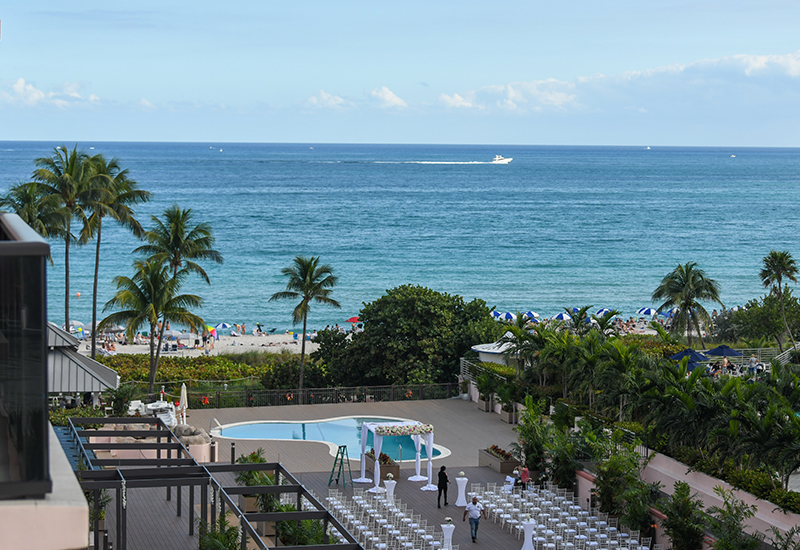 aerial image of the pool and a wedding being set up with the ocean in the background