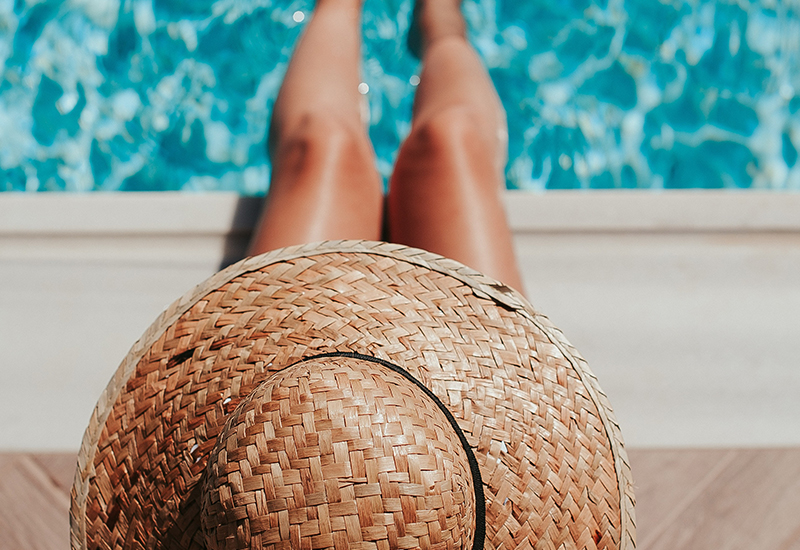 image from above a woman sitting with a sun hat while dipping her toes in the pool