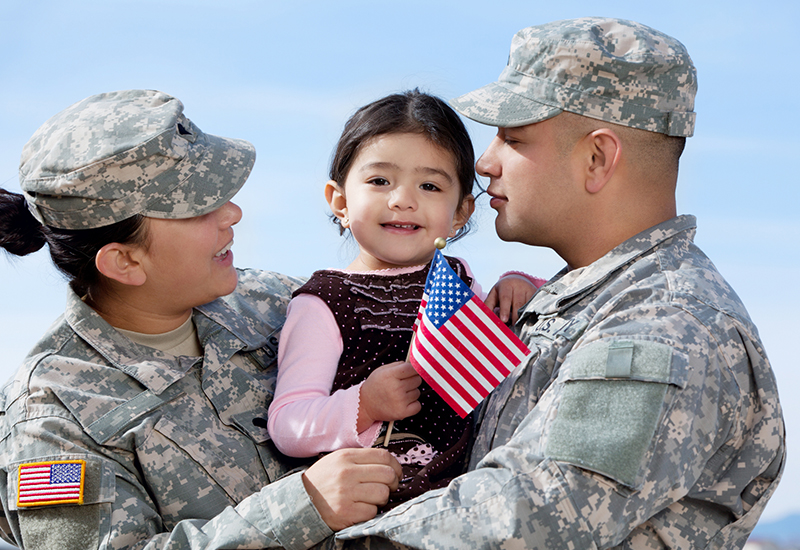 two people in military uniforms holding a little girl who is holding a small american flag