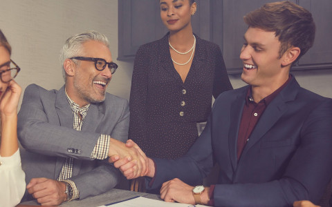 men dressed in suits shaking hands with two women watching them