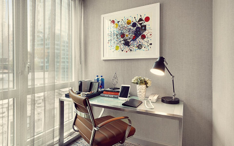 modern desk with a telephone, lamp and coffeemaker next to a large window. 