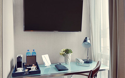A modern desk with flowers, lamp and coffee maker and a television on the wall