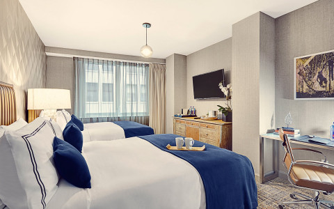 two queen bed hotel room with a large window, modern desk and chair, armoire and TV
