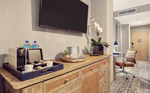 flat screen tv on the wall over an armoire with a coffee machine and ice bucket 