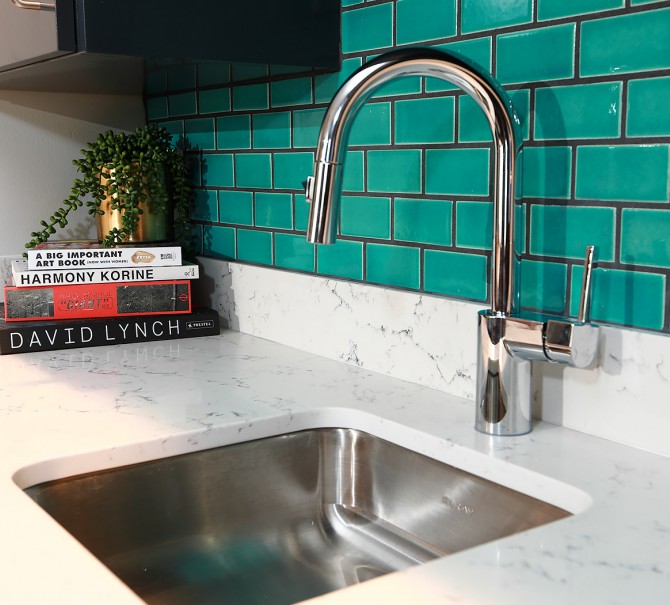 kitchen sink with teal blue wall tiles and a set of books in the corner below cabinet