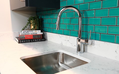 suite kitchen sink with teal blue tiled walls and books with a plant on top in the corner