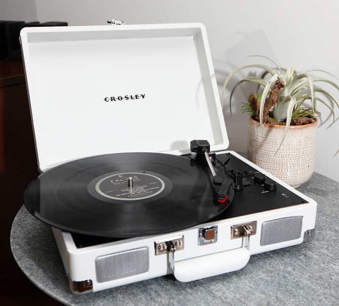 white crosley record player on small round grey table with a plant