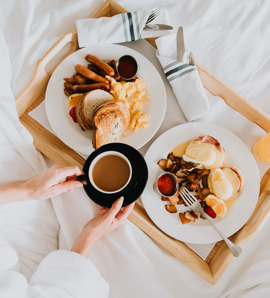 overhead view of a tray of breakfast food on white bed sheets