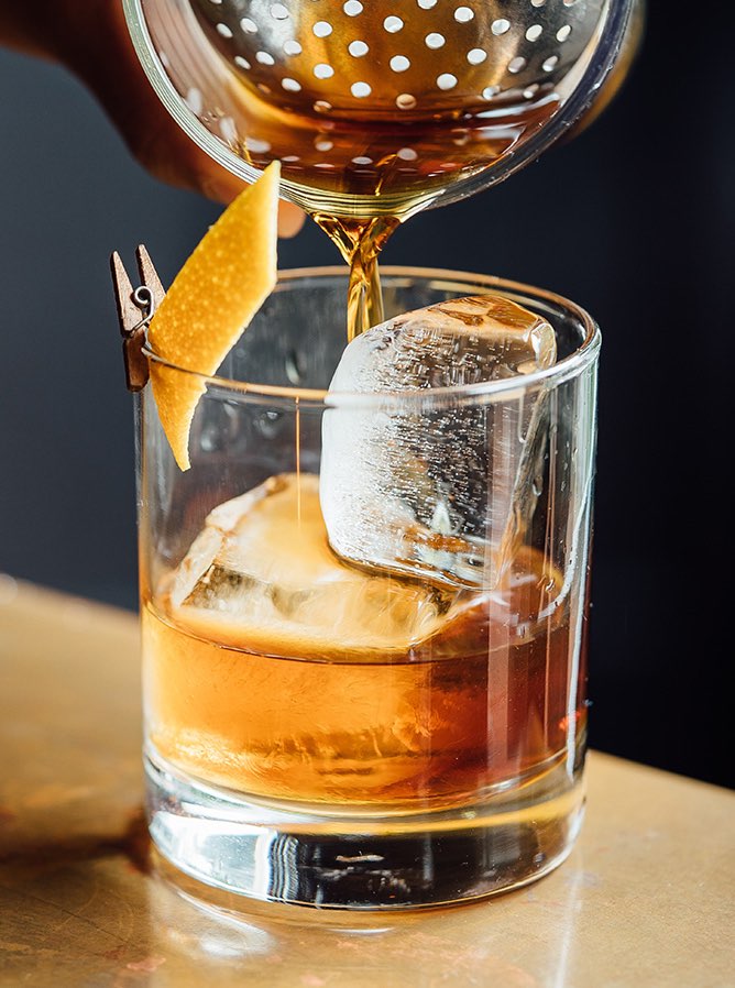 close up of a bourbon drink being poured into a glass from the cocktail shaker
