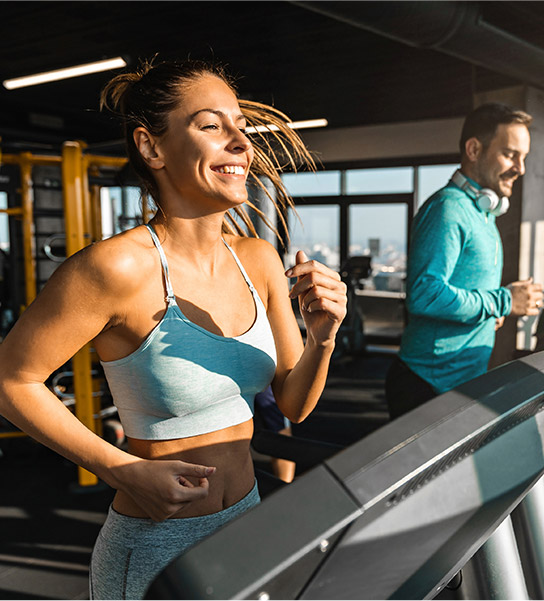 man and woman at the gym running on treadmills