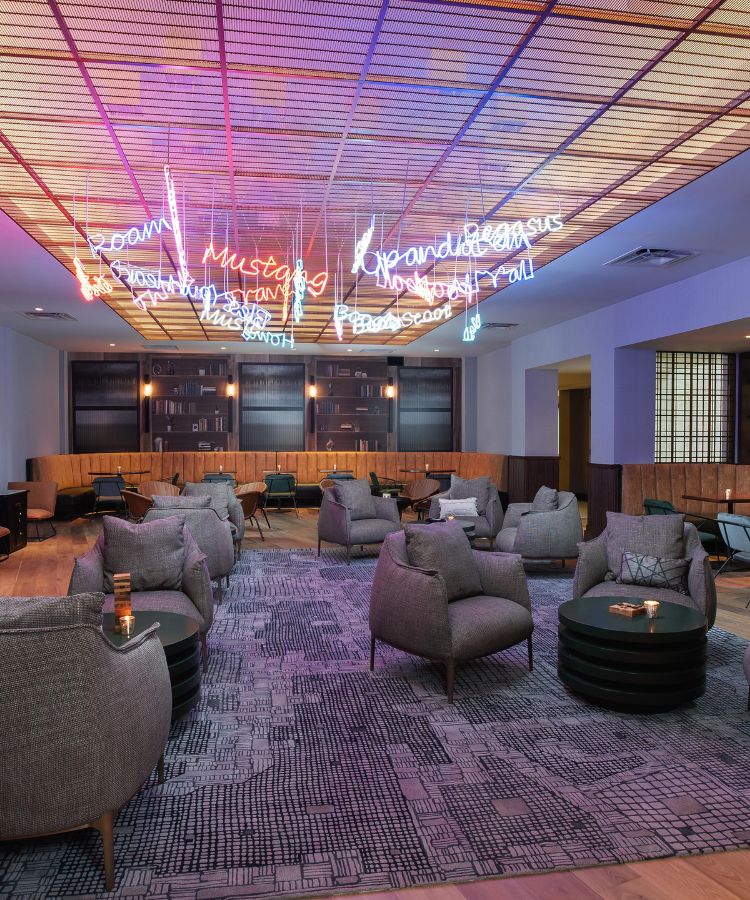rhapsody lounge venue with gray chairs in personal sitting areas, neon signs hanging from the ceiling and personal bookshelf towards the back of the wall.