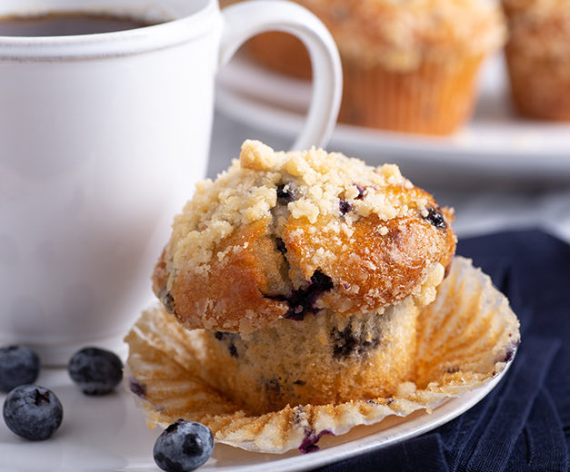a blueberry muffin with a coffee cup on a plate