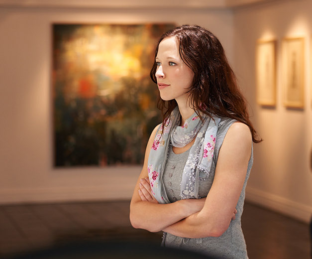 a woman crossing her arms looking at art in a museum 