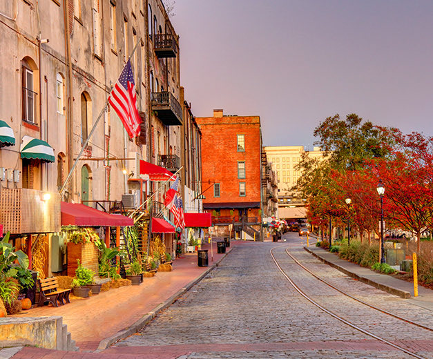a historic street with colorful trees a cobblestone street and the american flag hanging from a historic building