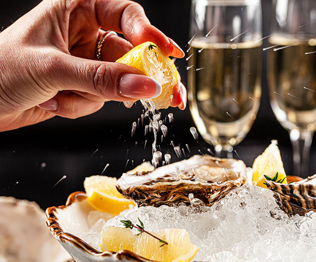 woman squeezing lemon over oysters with champagne glasses in the background