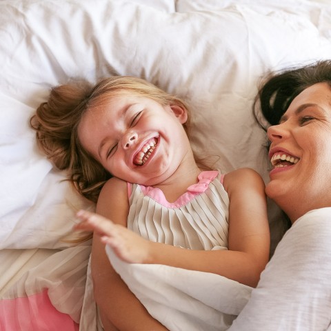women laying in bed with young daughter laughing