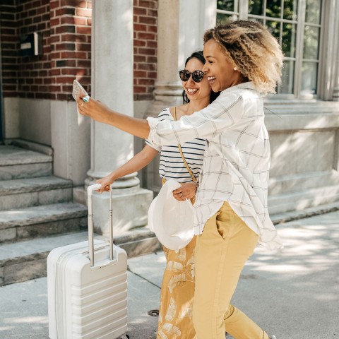 women walking in front of a building while walking with luggage and taking a picture