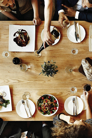 group of people sharing plate of cheese and salad at a white table