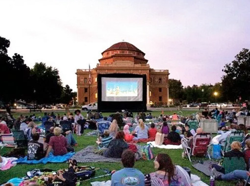 people sitting on a large field watching an outdoor movie screen