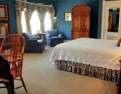 view of bedroom with white bed, desk with chair, two blue lounge chairs with table, armoire 