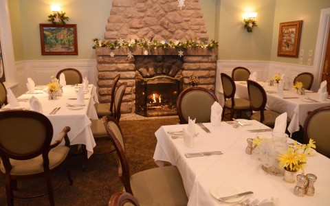 dining room with long white tables and tan chairs, fireplace in the background