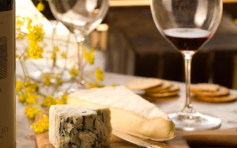 cheese plate with glasses of red wine in the background 