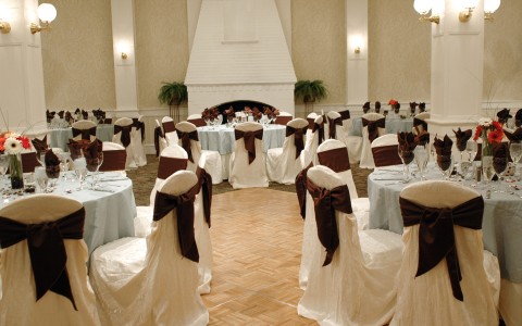 ballroom set up for a wedding with white circular tables and white chairs with maroon accents