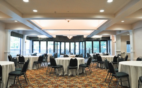 ball room set up with white circular tables and black chairs 