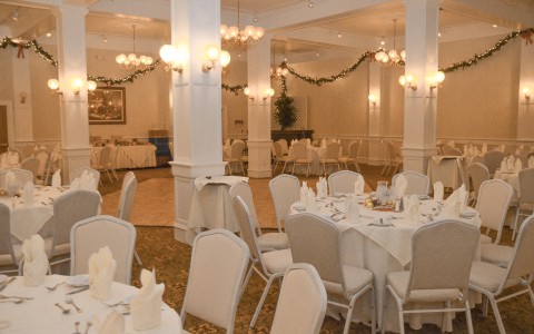 event room set up with dance floor, string lights around ceiling, circular white tables with chairs for a wedding 