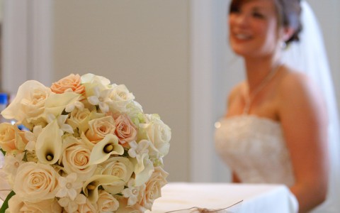 woman in a wedding dress smiling, bouquet of flowers in corner