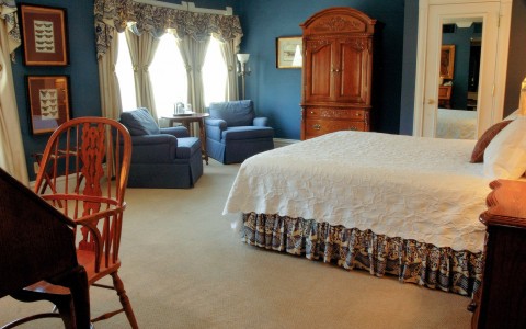 blue bedroom with white bed and floral accents, blue lounge chairs, dresser, desk with chair