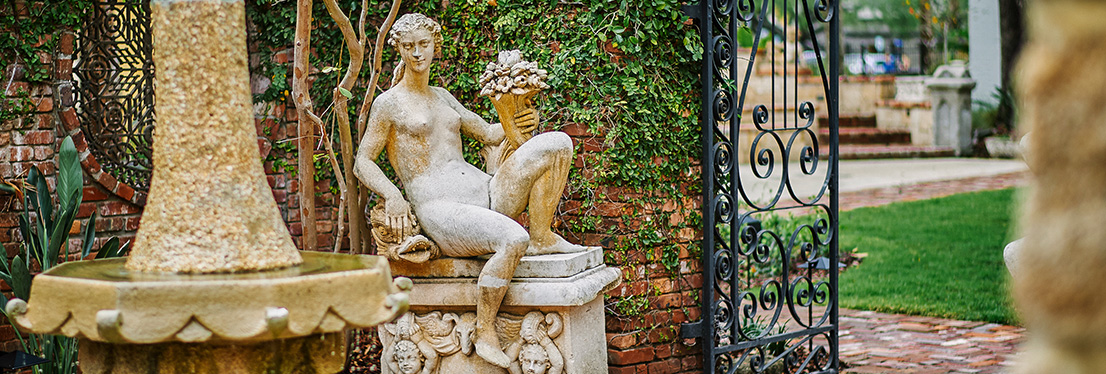 Outdoor statues in front of brick wall with ivy and a rod iron gate