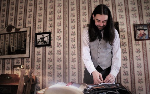 man with long hair folding clothes in a suitcase in his room 