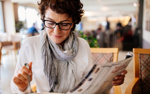 woman with short brown hair and glasses sitting at a table and holding a magazine