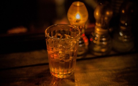 Close up image of a glass in the foreground with lightbulbs in the background