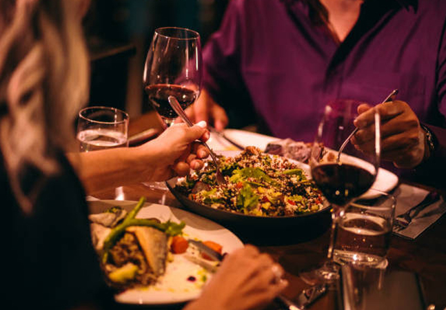 close up of two people eating at a table and two glasses of red wine