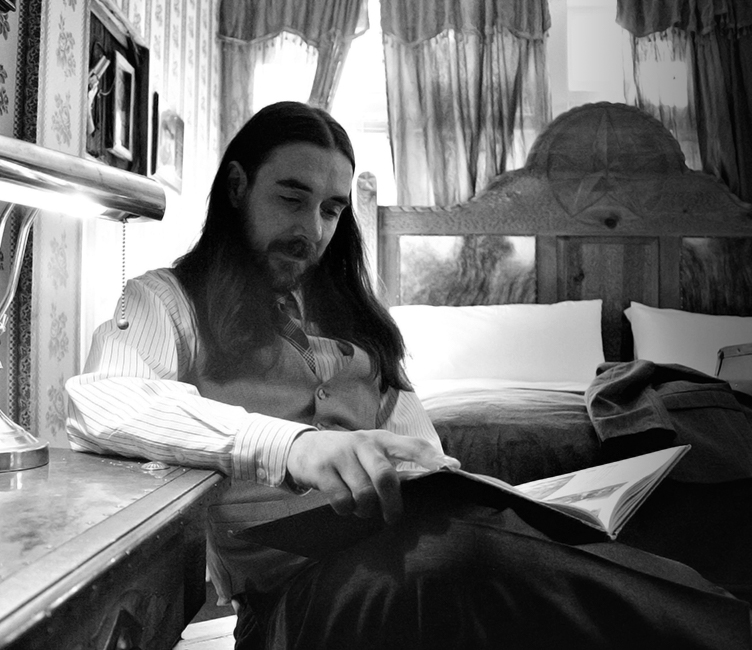 man with long hair and a mustache reading a book in black and white image