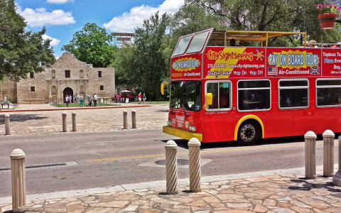 a red tourist bus driving in front of the alamo