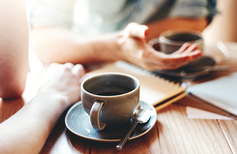 close up of two people's coffee mugs on a table at a coffee shop