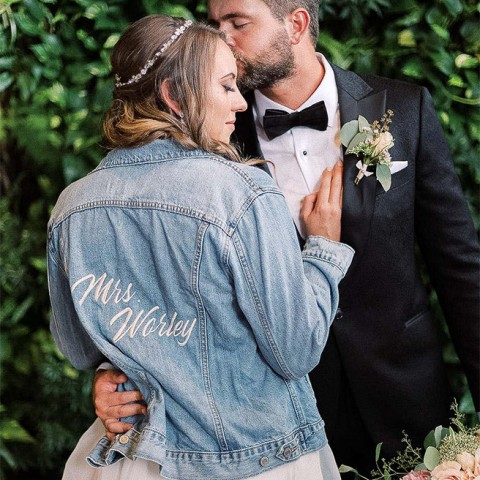 couple hugging and the bride is wearing a jean jacket with her new last name on it
