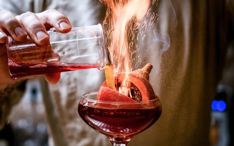 close up view of red cocktail with a flame
