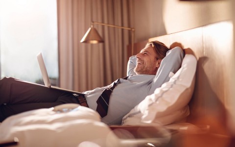 businessman laying in bed on his laptop laughing