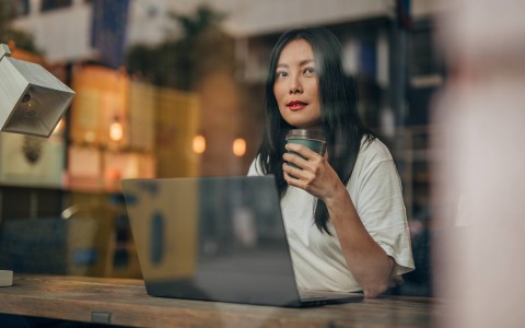 woman on her laptop drinking coffee and looking out the window