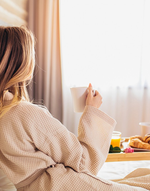 woman in a robe drinking coffee and eating breakfast in bed