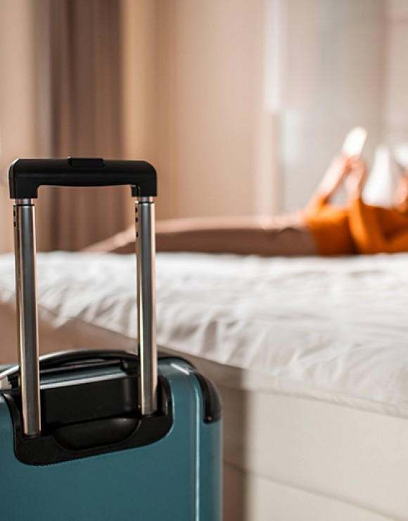 standing blue suitcase in front of a woman laying on the bed