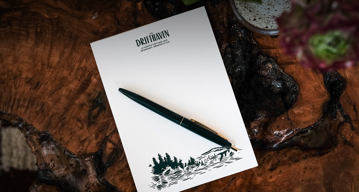 A drifthaven notepad and pen on top of a wood grain designed table.