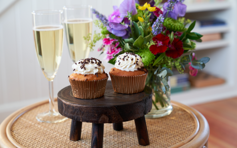 Two vanilla cupcakes topped with chocolate sprinkles and served with two glasses of champagne.