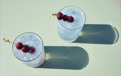 Two cocktails garnished with fresh cherries and the sun shining.